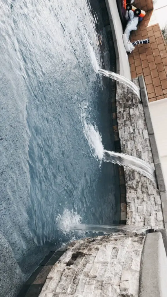 Swimming pool with three stone-clad water features creating streams of water along the pool wall.